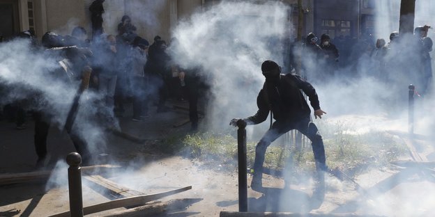 Vermummter in Rauch hebt Arm, um etwas zu werfen Vermummter in Rauch hebt Arm, um etwas zu werfen