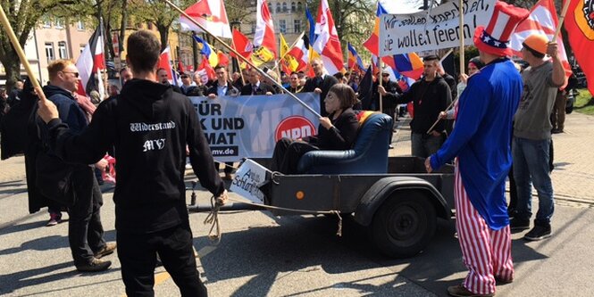 Demonstranten der NPD und eine Karren mit einer Figur, die Merkel darstellt