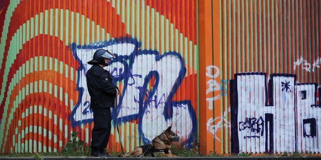 Ein Polizist mit Hund vor einer Wand mit Graffitis