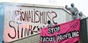 Menschen in Maleranzügen halten Bengalos und entrollen ein Transpi mit der Aufschrift „Stop Racial Profiling“