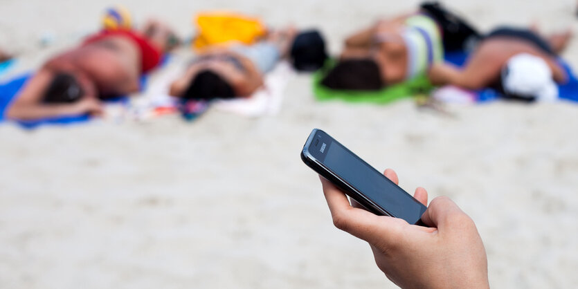 Eine Hand hält ein Handy am Strand