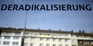 In einer Fensterscheibe steht das Wort „Deradikalisierung“, dahinter eine Häuserzeile