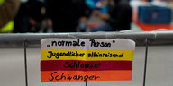 An einem Geländer hängen verschiedenfarbige Armbänder mit den Aufschriften „normale Person“, „Jugendlicher alleinreisend“, Schleuser“, „Schwanger“