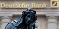 Statue mit nachdenklichem Blick, im Hintergrund das Logo der Deutschen Bank