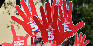 Streikende halten rote Schilder in Form von Händen in die Höhe, auf denen „Wir für 5“ steht