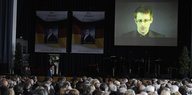 Menschen sitzen in einem Saal, an der Wand eine Leinwand mit dem projizierten Konterfei Edward Snowdens