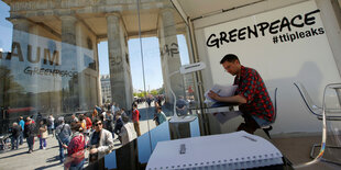 Mann sitzt im Greenpeace-Glaskasten vor dem Brandenburger Tor und nimmt Einblick in die geleakten Papers