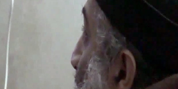 Osama bin Laden mit weißem Bart und schwarzer Mütze schaut vom rechten Bildrand nach links hinten
