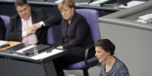 Sarah Wagenknecht spricht im Bundestag. Sigmar Gabriel und Angela Merkel sitzen im Hintergrund und hören zu.