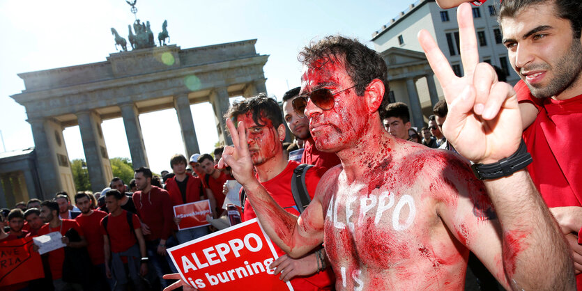 Mit roter Farbe bemalter Mann beim Aleppoisburning-Protest vor dem brandenburger Tor