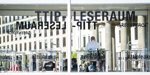 Ein Mensch sitzt in einem gläsernen Raum mit der Aufschrift "TTIP-Leseraum"