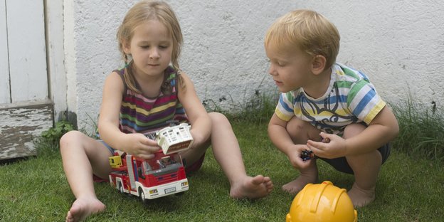 Ein Junge und ein Mädchen spielen mit einem Feuerwehrauto.