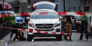 Um einen weißen Mercedes-Geländewagen stehen ein paar Polizisten zur Spurensicherung.