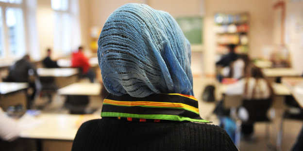Eine Frau mit Kopftuch von hinten in einem Klassenzimmer