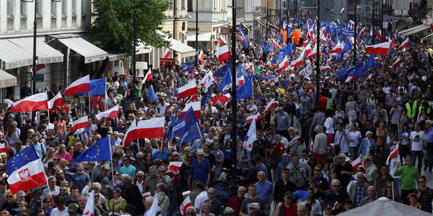 Menschen sind auf der Straße zu sehen mit Polen-Flaggen und Europa-Flaggen