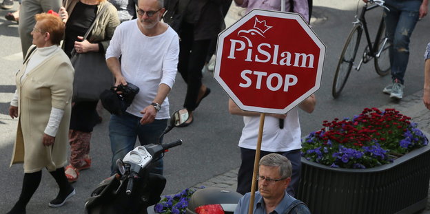 Demonstrant hält ein Schild mit „PiSlam Stop“ hoch.