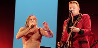 Zwei Männer auf einer Bühne: Einer singt und ist oberkörperfrei, es ist Iggy Pop, der andere trägt einen roten Anzug, singt und spielt Gitarre, es ist Josh Homme.