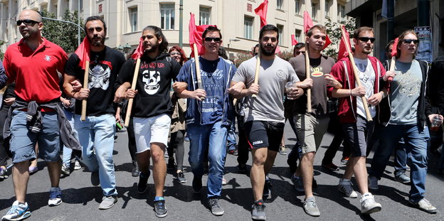 Ein Gruppe junger Männer geht in einer Reihe eine Straße entlang, alle tragen Flaggen zum Schwenken mit.