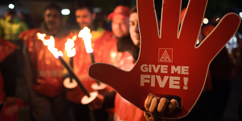 Beschäftigte der Metall-Industrie in Köln streiken. Sie halten Feuer und ein Plakat in der Hnad, fordern give me five