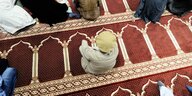 Ein Kind sitzt in einer Moschee auf dem Teppich