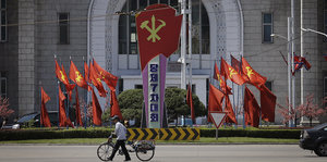 Ein Mann mit Fahrrad läuft an einem Haus und Fahnen der Nordkoreanischen Arbeiterpartei vorbei