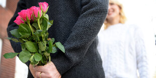 Ein Mensch hält einen Blumenstrauß hinter dem Rücken