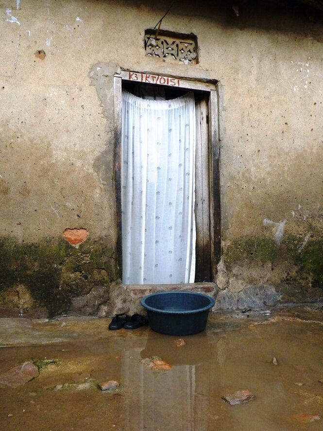 Eine Haustr mit Vorhang. Davor ein Eimer auf dem Boden der Regenwasser sammelt