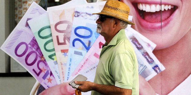 Ein vor einem Wandposter auf dem eine lächelnde Frau Geldscheine in der Hand hält