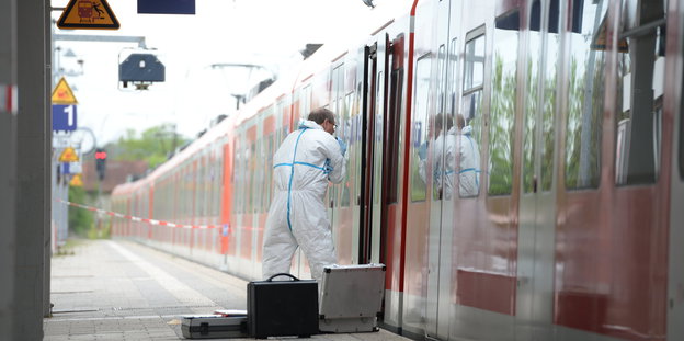 Am S-Bahnsteig Grafing steht ein Ermittler in weißem Schutzanzug vor einer S-Bahn, neben ihm verschiedene Koffer