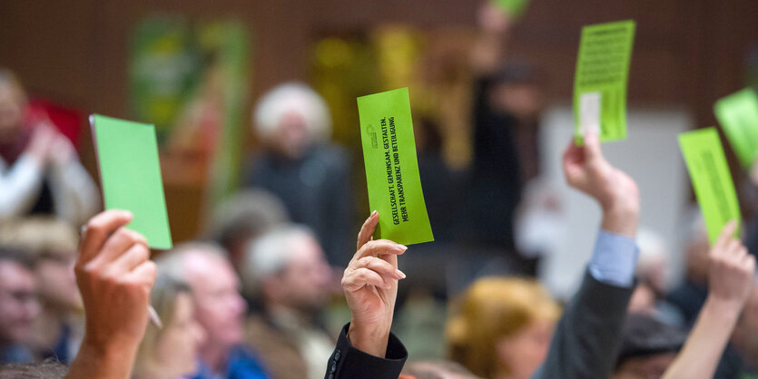 Menschen heben ihre Arme, in den Händen halten sie grüne Zettel