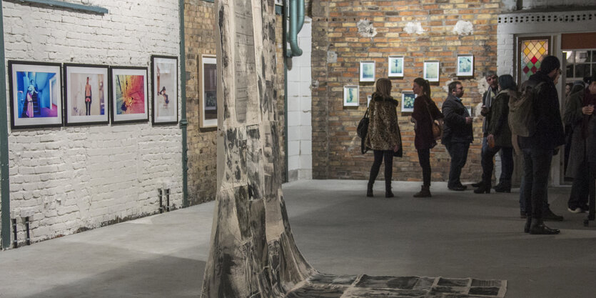 Menschen, die bei einer Ausstellung in einer alten Lagerhalle Kunstwerke betrachten