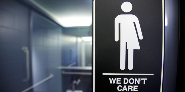 Ein Schild in einer Toilette zeigt die eine Person, deren Geschlecht nicht eindeutig ist und die Aufschrift „We don't care“