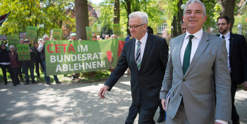 Winfried Kretschmann und Thomas Strobel laufen an Ceta-Gegner_innen vorbei