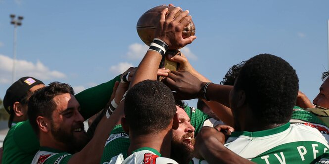 Rugbyspieler drängen sich aneinander und halten einen Rugbyball in die Luft