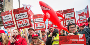 Männer und Frauen mit Trillerpfeifen und Schildern sowie einem Plastikhai