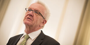 Ein Mann blickt aus dem Bild. Es ist Winfried Kretschmann