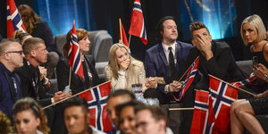 Eine Gruppe von Menschen hält norwegische Flaggen in den Händen und hat schockierte Gesichtausdrücke