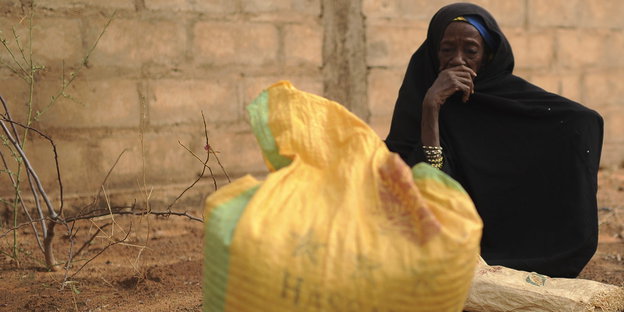 Eine nigerianische Frau trägt ein schwarzes Gewand und hockt vor einem Sack Reis