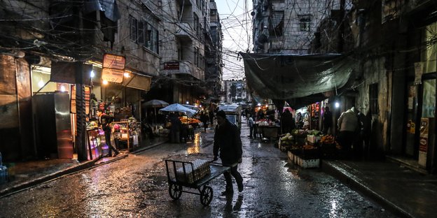 Ein Mann schiebt einen Handwagen durch eine Einkaufsstraße in Aleppo. Es regnet stark