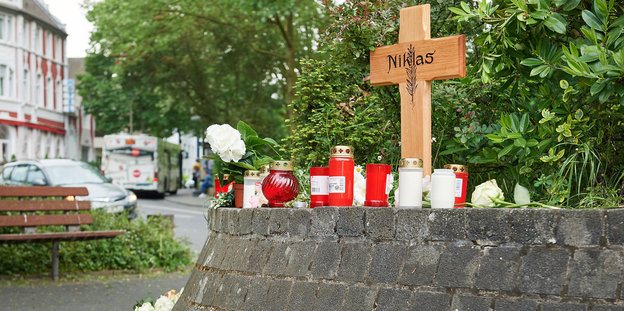 ein Kreuz mit der Aufschrift "Niklas" und Kerzen, im Hintergrund eine Straßenszene