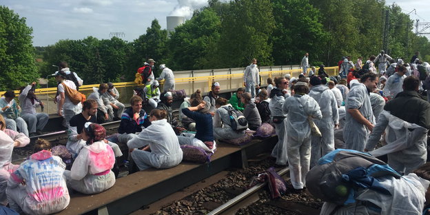 Menschen in Schutzanzügen sitzen auf Bahnschienen