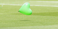 Ein grüner, herzförmiger Luftballon schwebt über Fußballrasen