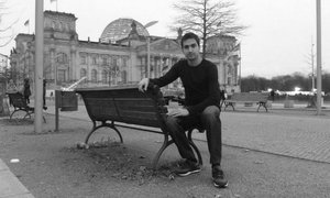 Mawlud sitzt auf einer Bank vor dem Reichstagsgebäude