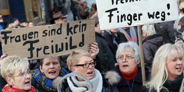 Frauen protestieren auf der Straße, sie halten Schilder auf denen "Finger weg" und "Frauen sind kein Freiwild" stehen