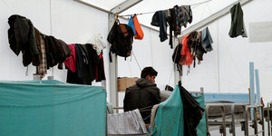 Ein Flüchtling sitzt in Schisto in einem UNHCR-Zelt unter trocknender Wäsche