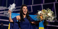 Die ESC-Gewinnerin Jamala hält lachend einen Pokal und einen Blumenstrauß