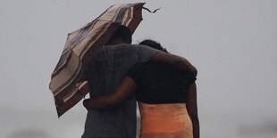 zwei Menschen Arm in Arm unter einem Regenschirm