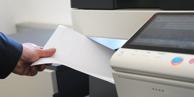 Eine Hand zieht von links ein Blatt aus einem Kopiergerät