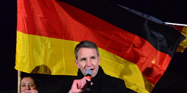 ein Mann mit Mikrofon vor einer Deutschlandfahne