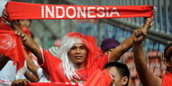 ein Mann mit rot-weißer Perrücke hält einen roten Schal hoch, auf dem „Indonesia“ steht